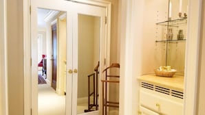 A hallway with a mirrored closet door, a wooden chair, and a vanity with a mirror and shelves.
