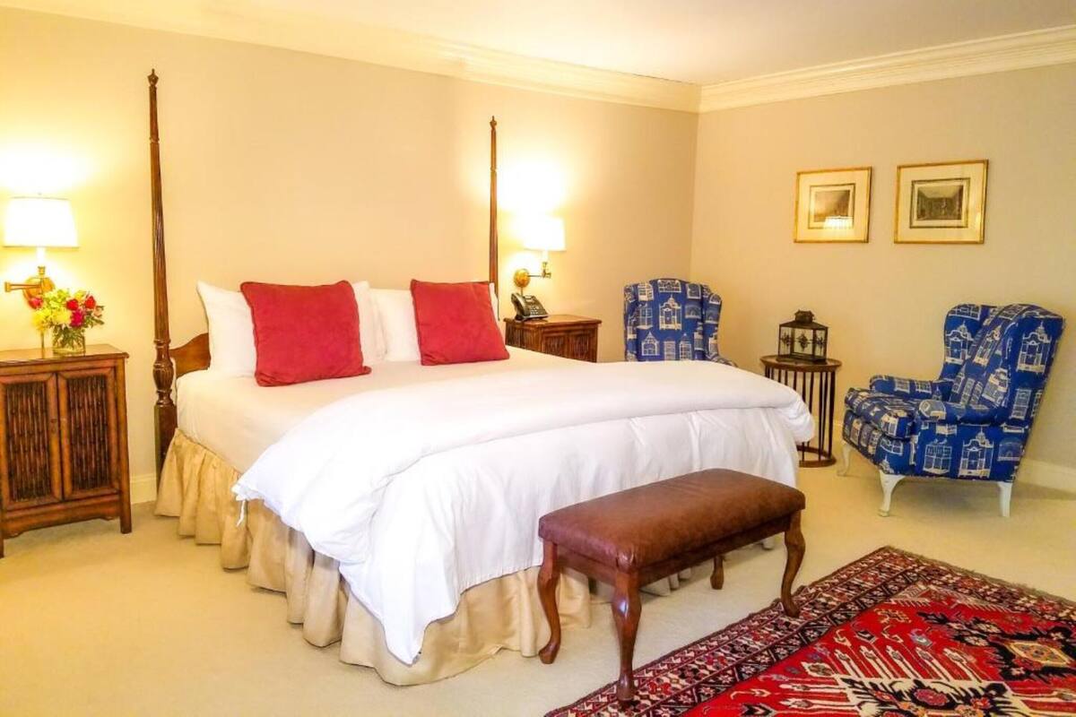 A spacious bedroom with a large bed, a bench, two chairs, and a patterned rug.