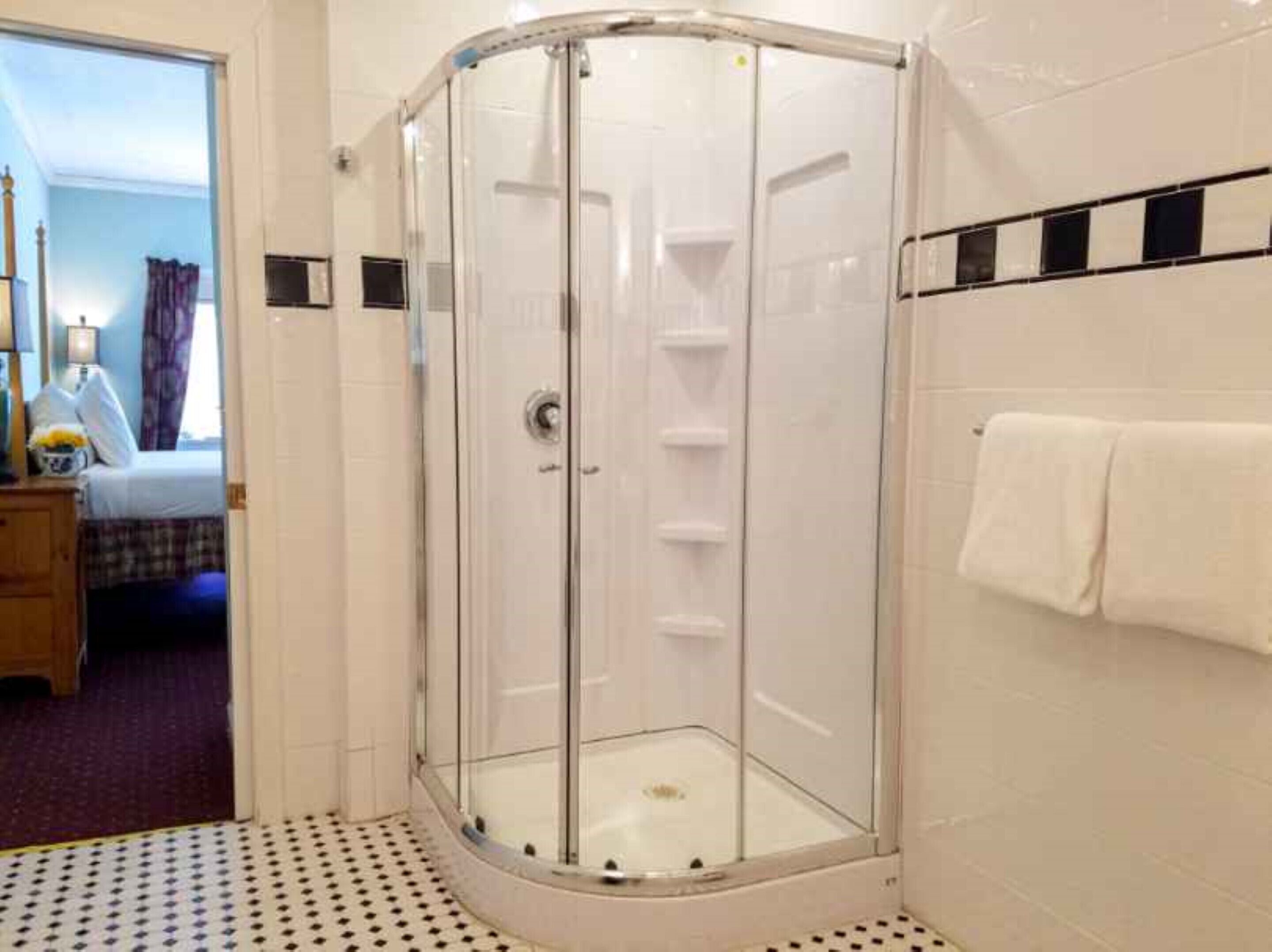 Een douche met glazen wand, een witte betegelde muur en een handdoek aan de muur.