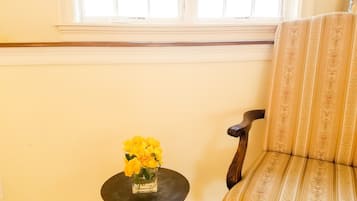 A room with a window, a chair, and a small table with a vase of yellow flowers.