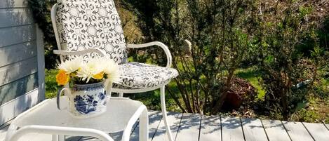 Una terraza blanca con una silla metálica blanca y una maceta cerámica azul y blanca con flores.