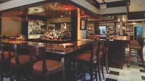 A bar area with a long counter, multiple stools, and a well-stocked bar.