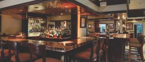 Zona de bar con una barra larga, varios taburetes y una amplia selección de bebidas.