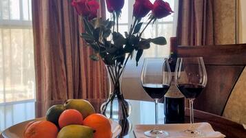 Une table avec un panier de fruits, un vase de roses et deux verres à vin.