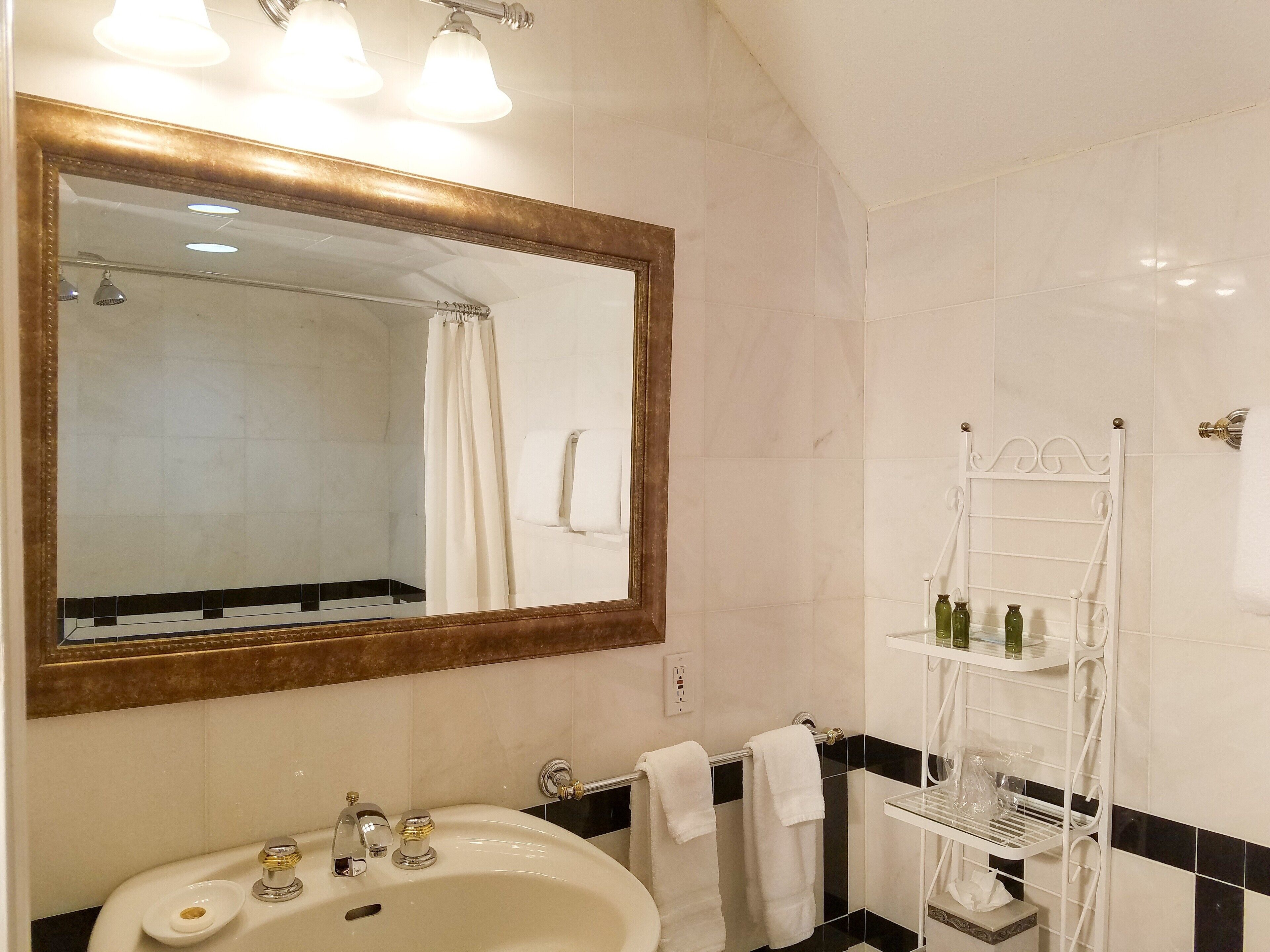 A bathroom with a large mirror, a sink, a shower, and a towel rack.
