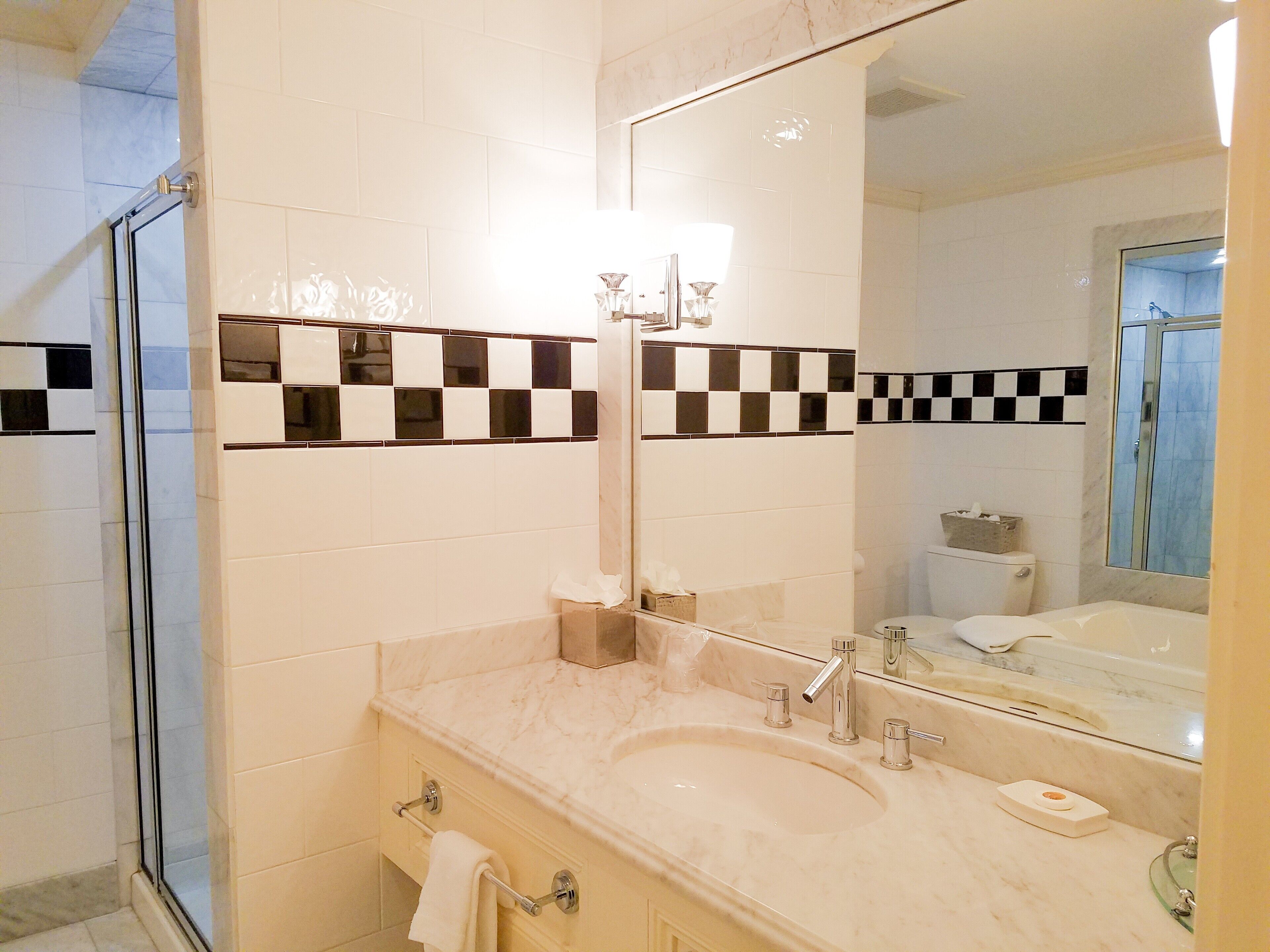 A bathroom with a large mirror, a sink with two faucets, and a glass shower enclosure.