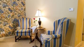 Una habitación con dos sillones a rayas, una pequeña mesa con una lámpara y un papel tapiz floral.