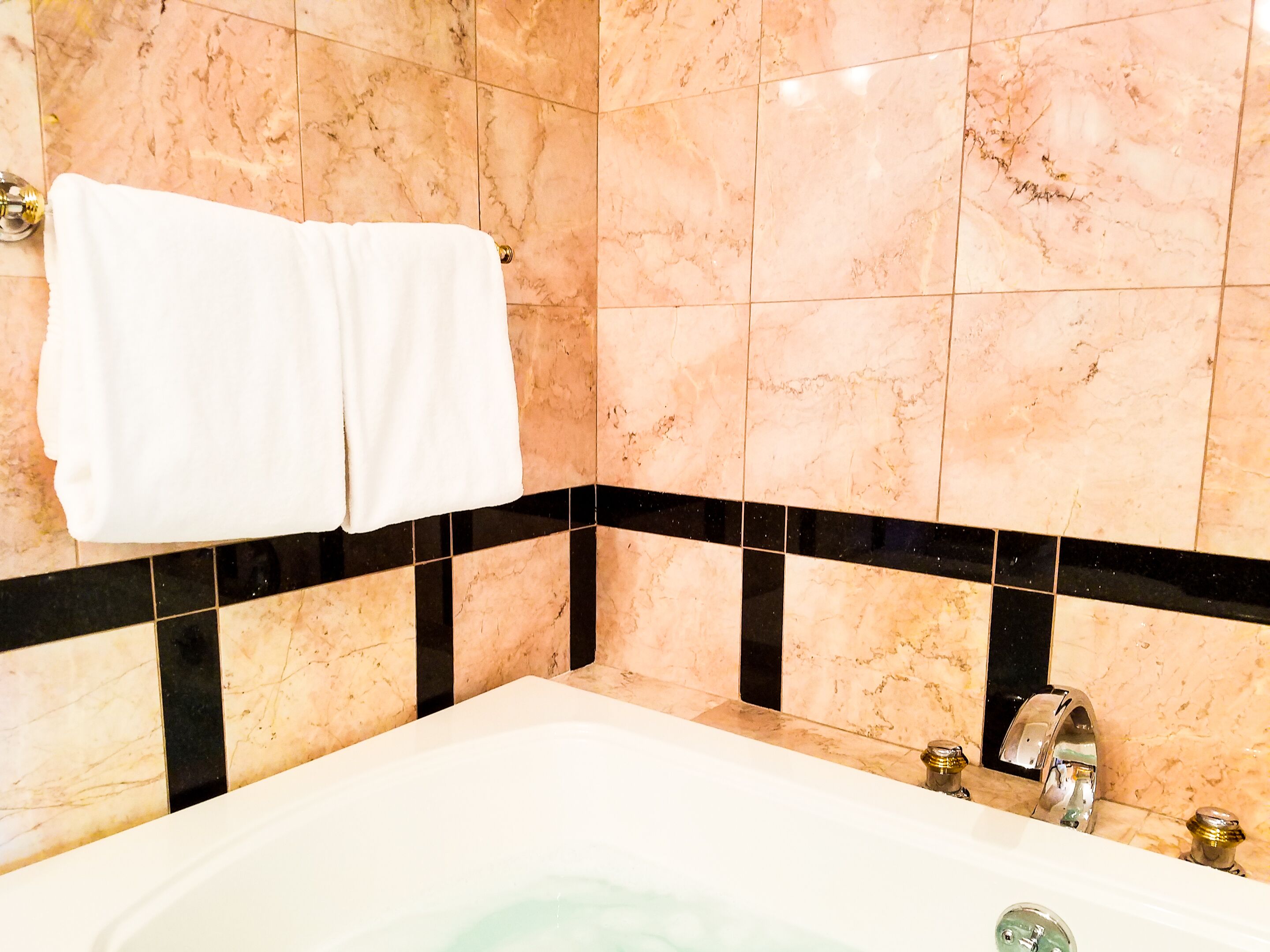 A bathroom with a bathtub, marble walls, and black and beige tiles.