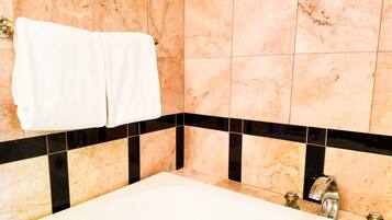 A bathroom with a bathtub, marble walls, and black and beige tiles.