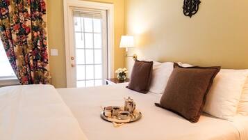 A hotel room with a bed, a tray with a teapot and cups, a lamp, and a floral curtain.