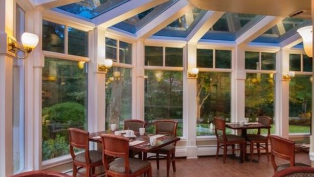 A conservatory with a glass ceiling, wooden furniture, and large windows offering a view of the garden.