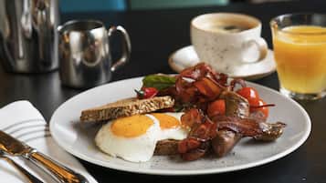 A breakfast plate with eggs, bacon, tomatoes, and toast, accompanied by a coffee cup and a glass of orange juice.