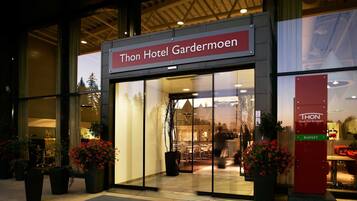 Thon Hotel Gardermoen features a modern entrance with a large glass facade and potted plants on either side.