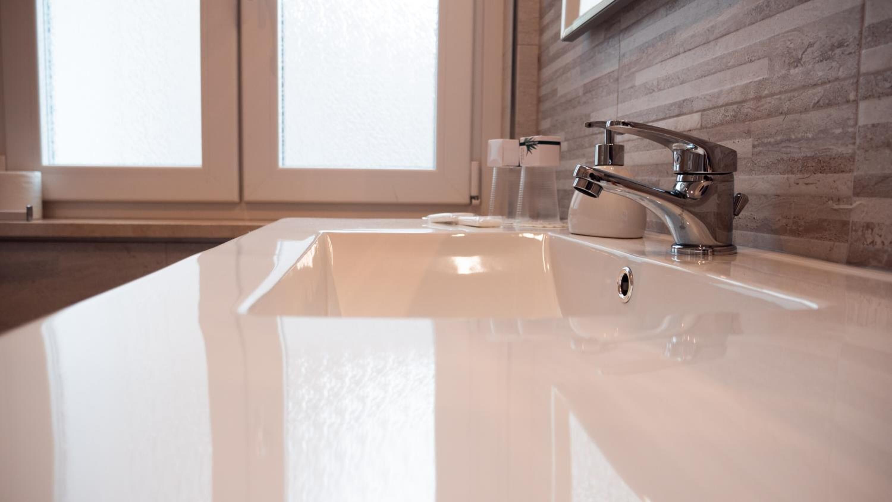 Un baño moderno con un lavamanos blanco, grifo cromado y un vaso de agua.