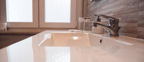 Un baño moderno con un lavamanos blanco, grifo cromado y un vaso de agua.
