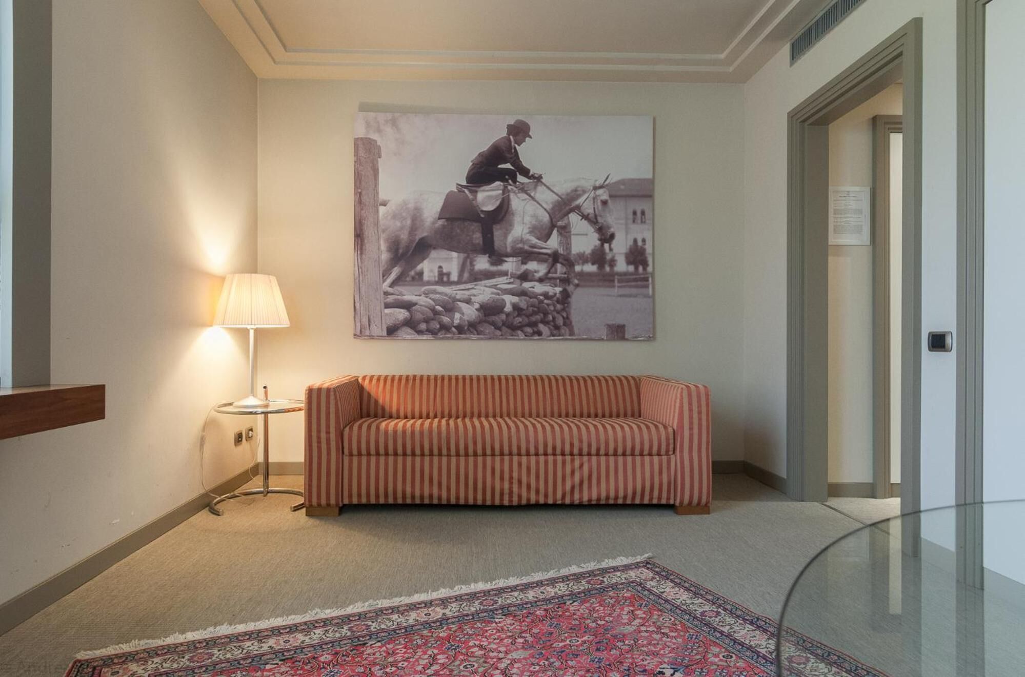 En hall med en randig soffa, en lampa, en stor inramad tavla och en mönstrad matta.