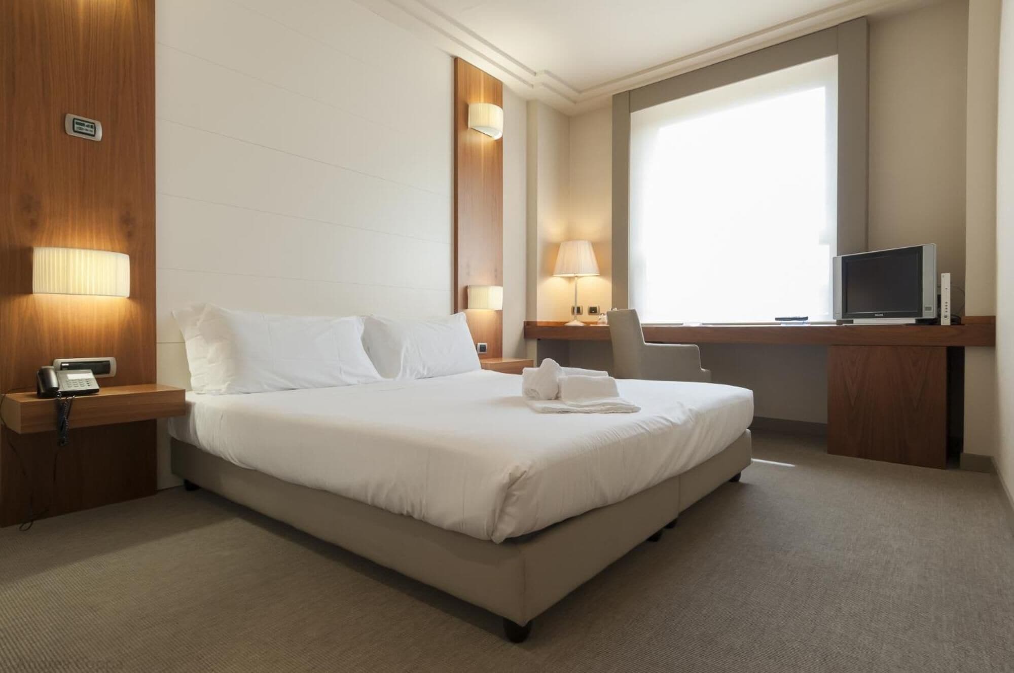 Habitación de hotel con una cama grande, lámparas de noche, un escritorio con televisor y una ventana.