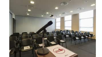 Une salle de conférence avec des rangées de chaises, un pupitre et une grande fenêtre.