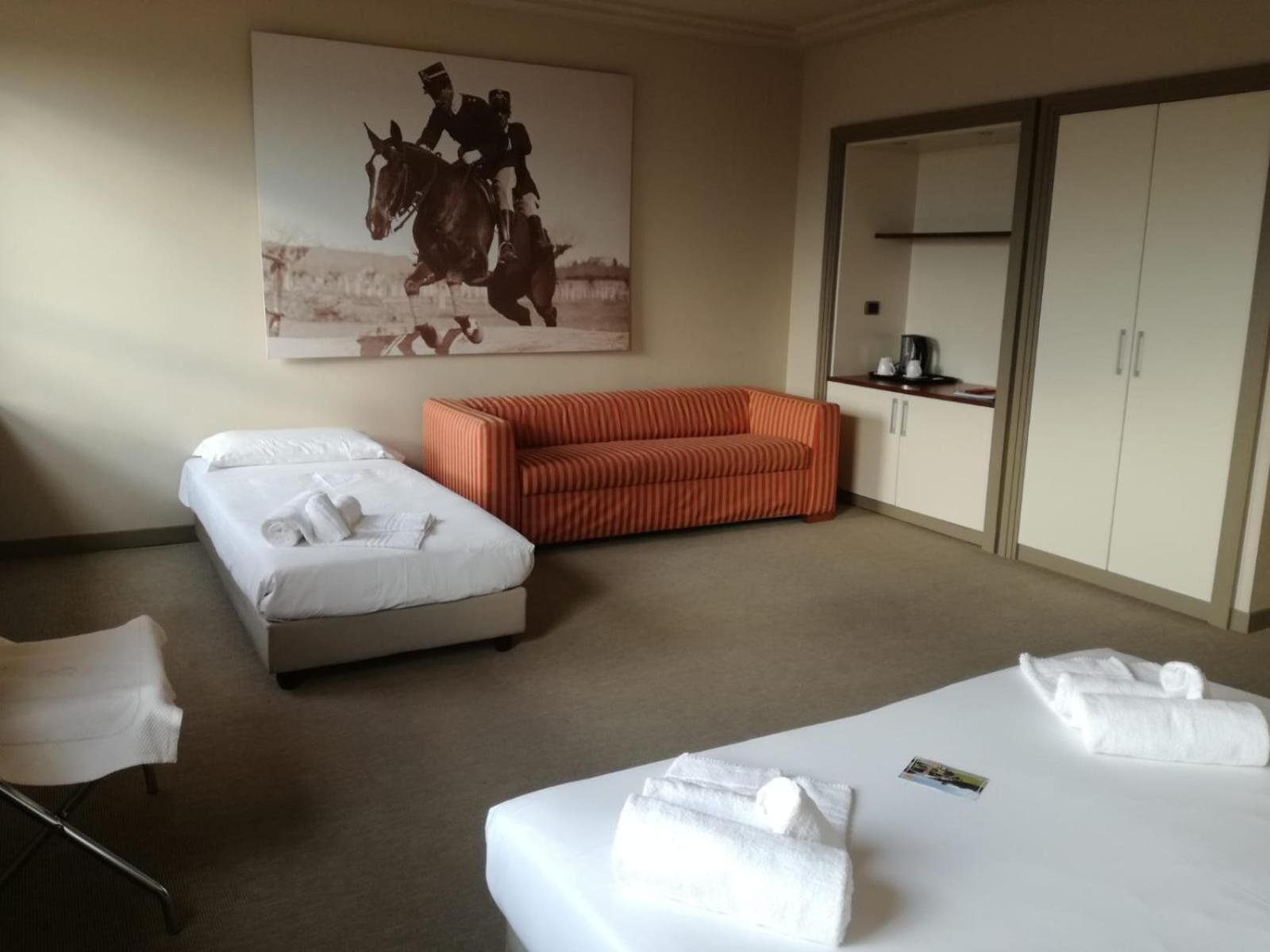 Habitación de hotel con dos camas, un sofá, un armario y un cuadro en la pared.