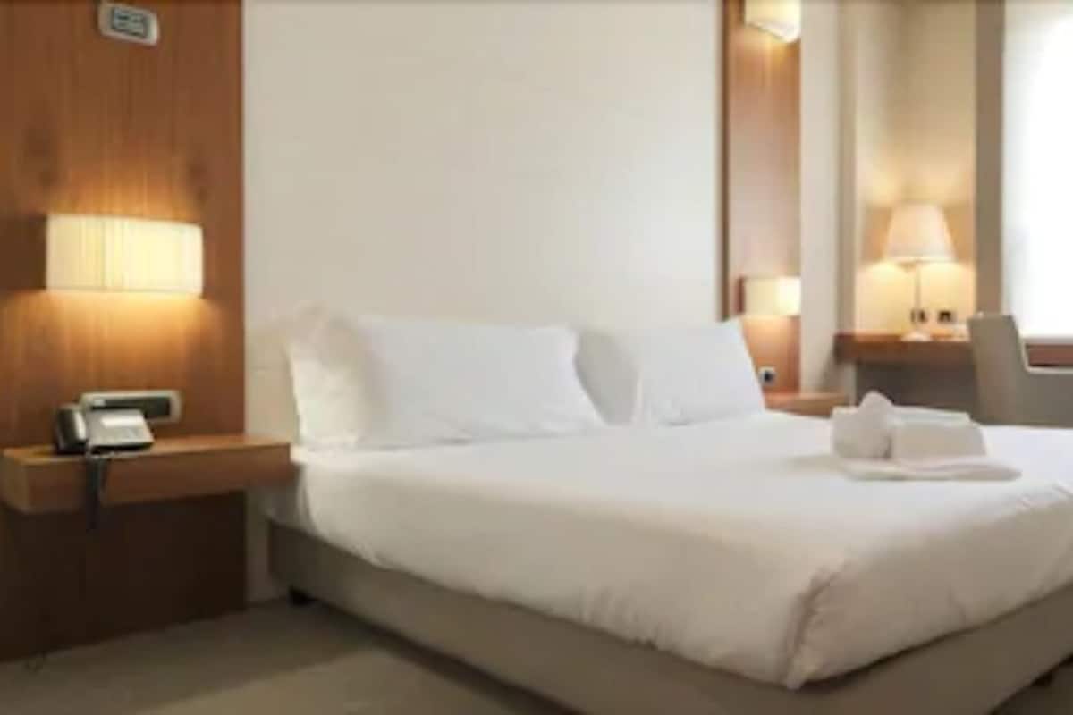 A hotel room with a bed, bedside lamps, a TV, and a desk.