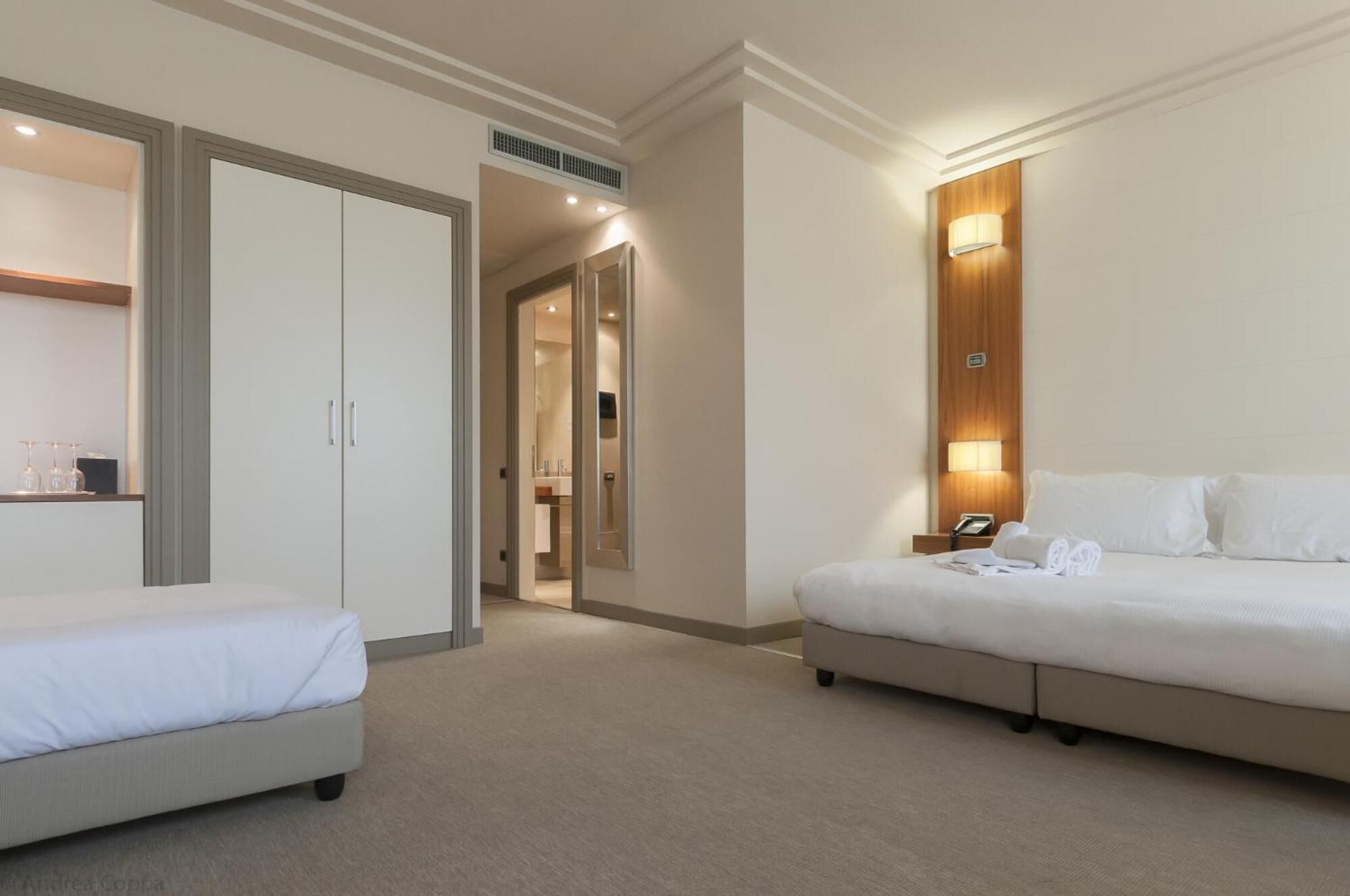A hotel room with a bed, a smaller bed, a wardrobe, and a bathroom visible through an open door.