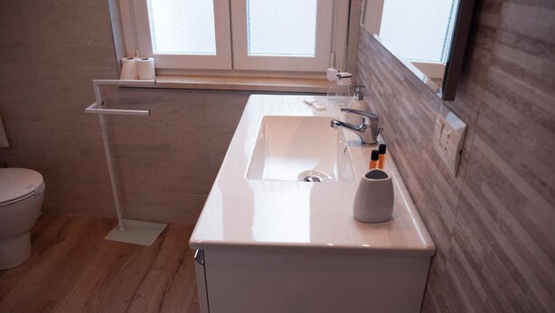 Une salle de bain moderne avec un lavabo blanc, des toilettes et une fenêtre située au-dessus du lavabo.