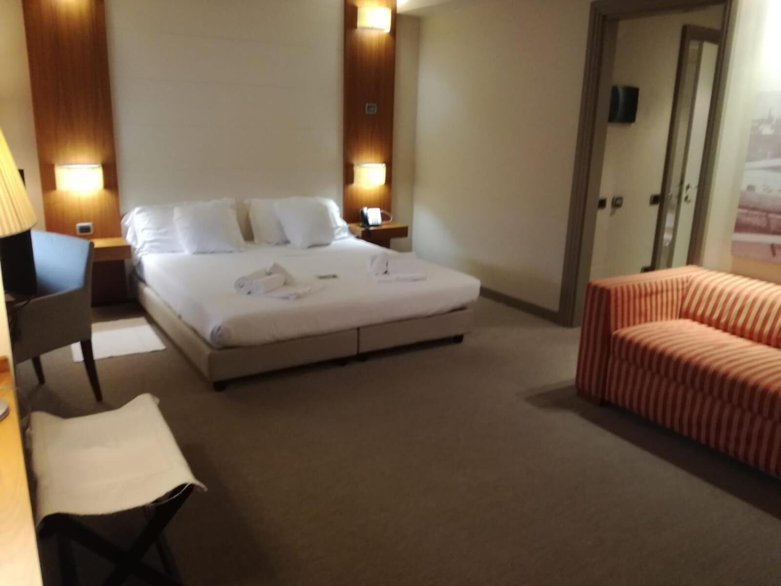 Une chambre d’hôtel avec un grand lit, des lampes de chevet, un bureau et un canapé à rayures.