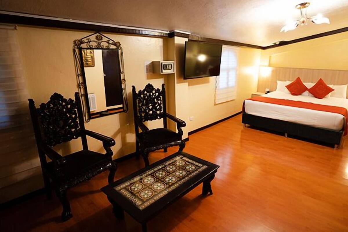 Habitación de hotel con una cama, dos sillas, una mesita, un televisor y una ventana.