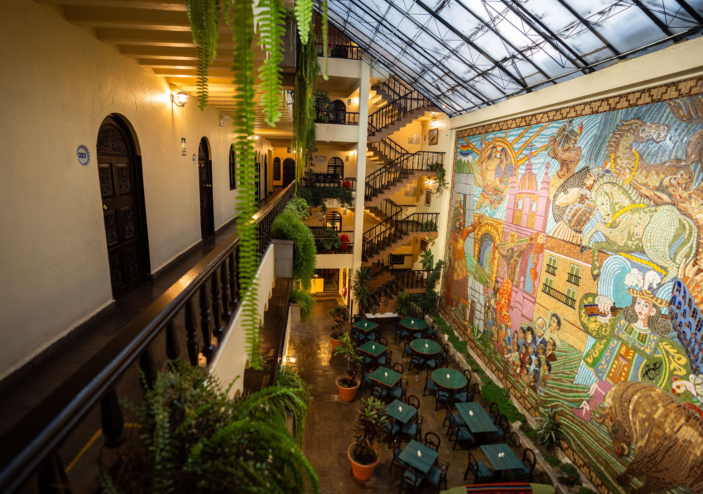 A multi-level atrium with a glass ceiling, indoor plants, and a large mosaic mural.