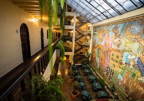 A multi-level atrium with a glass ceiling, indoor plants, and a large mosaic mural.