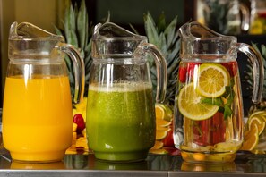Three pitchers of different colored beverages, each with a handle and spout, placed on a reflective surface. - Nodo Cusco Santa Teresa (Cusco)