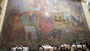 Een eetgedeelte met mozaïekkunst op de muur en gedekte tafels.
