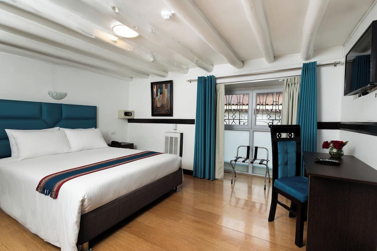 A hotel room with a large bed, a desk, a chair, and a view of the outside.