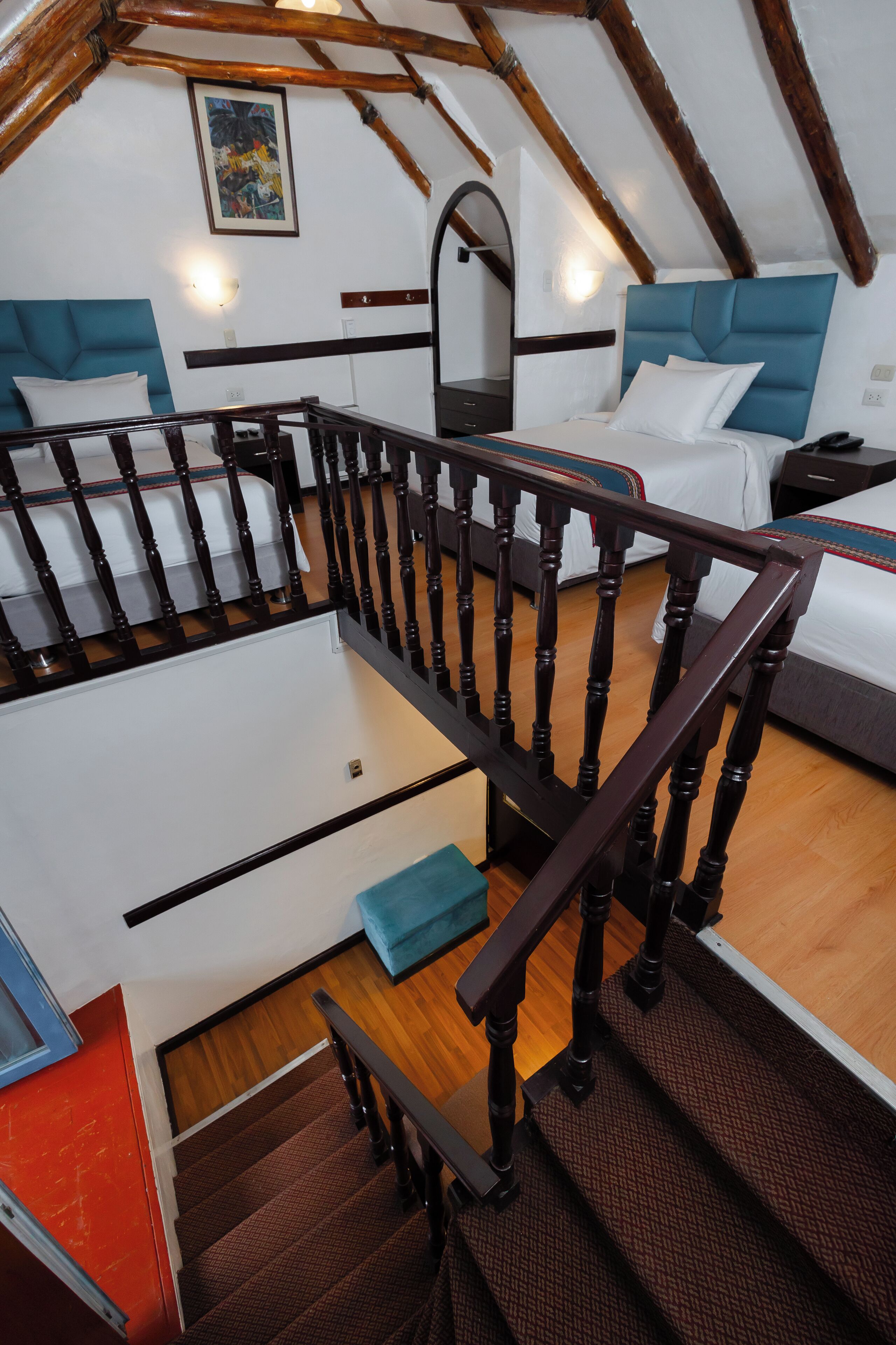 Un dormitorio estilo loft con escalera de madera, cama con cabecera azul y un cuadro en la pared.