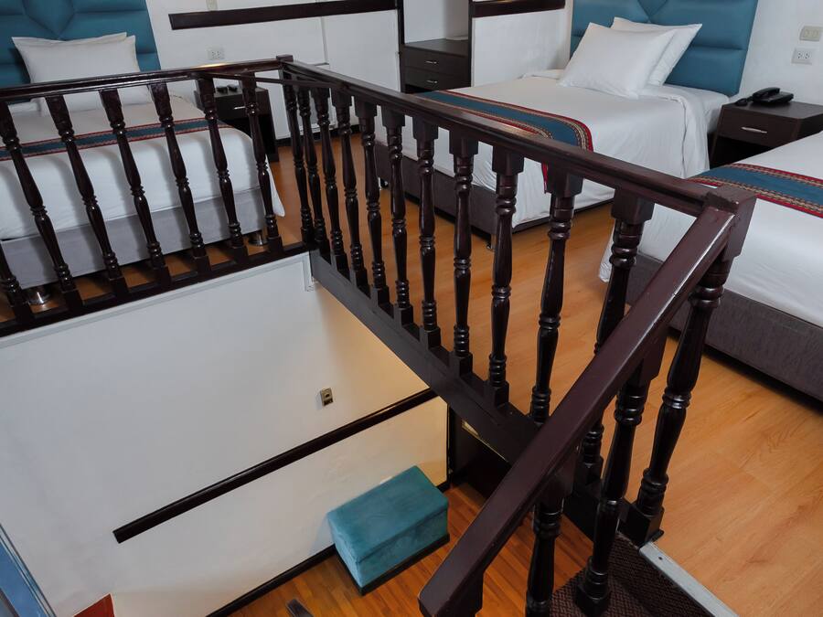 Un dormitorio estilo loft con escalera de madera, cama con cabecera azul y un cuadro en la pared.