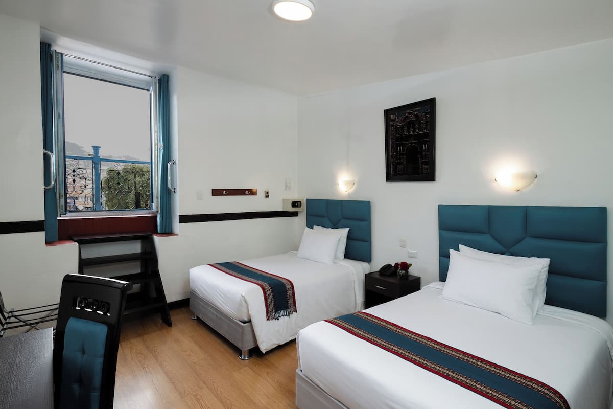 A hotel room with two beds, a desk, a chair, and a window with curtains.