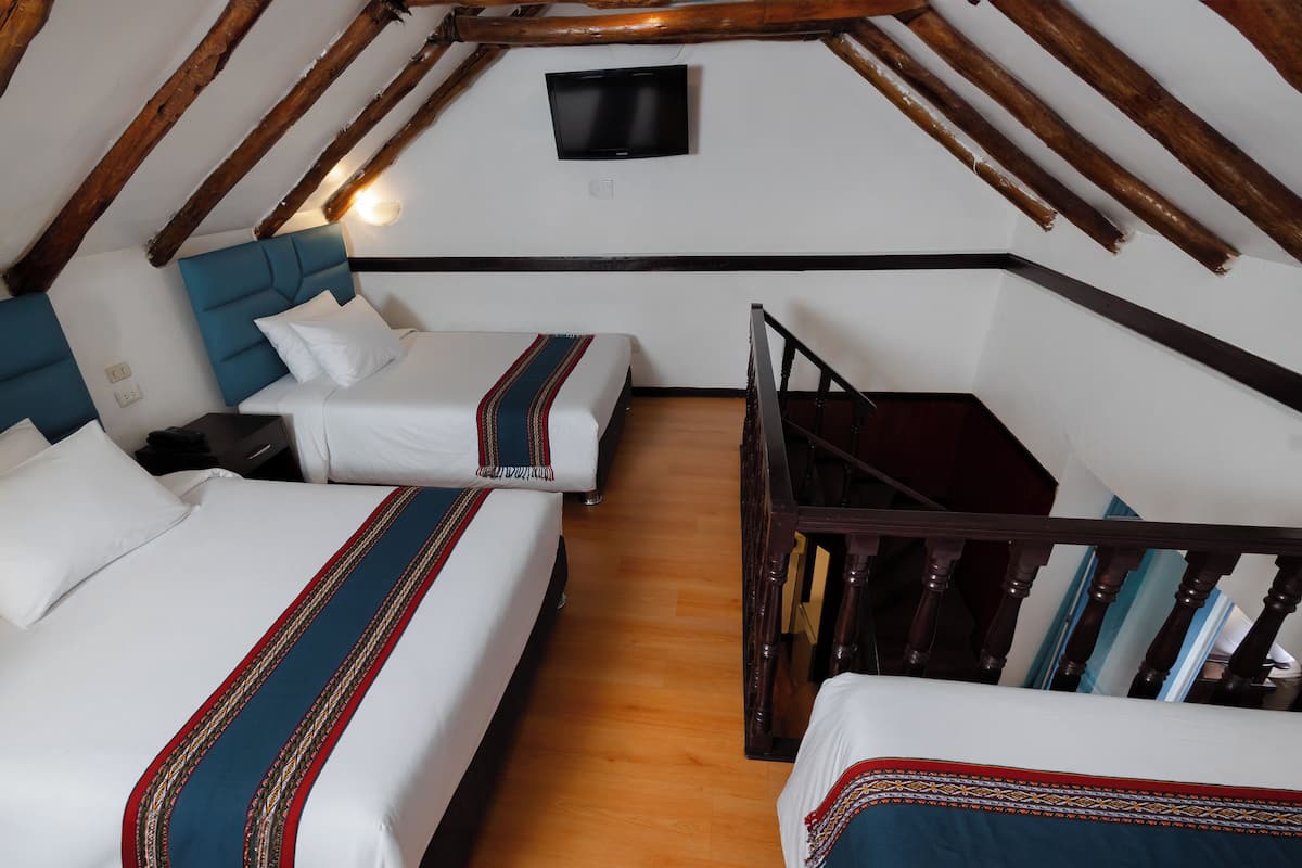 A room with two beds, a wooden ceiling, and a TV mounted on the wall.