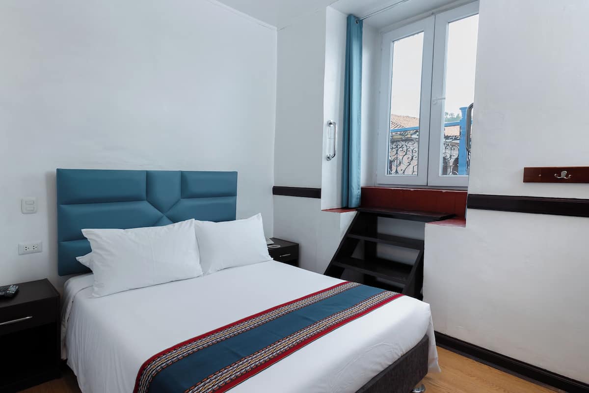 A hotel room with a bed, a nightstand, a window with curtains, and a view of the outside.