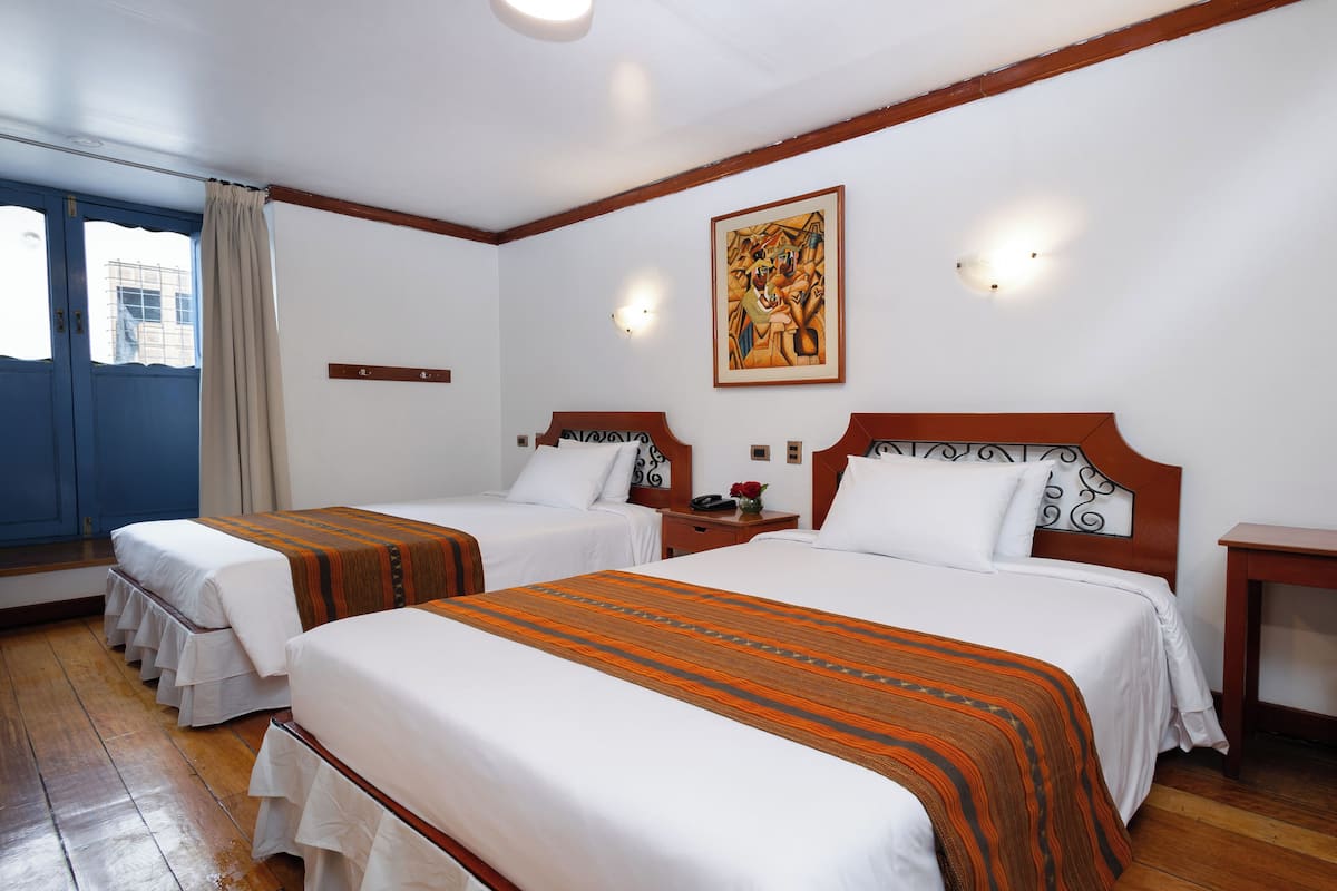 A hotel room with two beds, wooden headboards, white bedding, a painting on the wall, and a wooden floor.