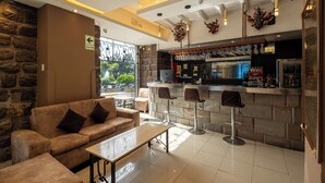 A bar area with a stone wall, a sofa, and two bar stools. - Hotel Hacienda Cusco Plaza (Cusco)