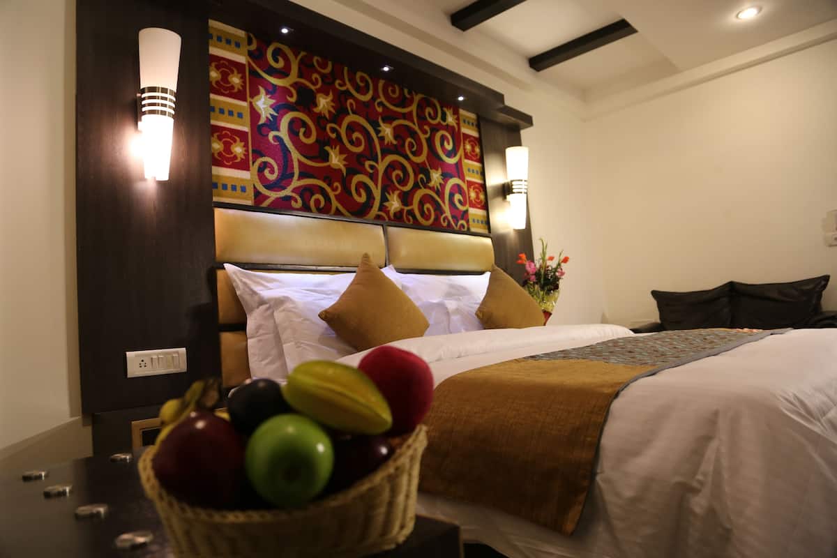 Une chambre d’hôtel avec un grand lit, une tête de lit décorative, un luminaire fixé au mur et un panier de fruits sur la table de chevet.