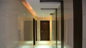 A modern hallway with a wooden door, glass walls, and a tiled floor. - Hotel Sri Nanak Continental (New Delhi)
