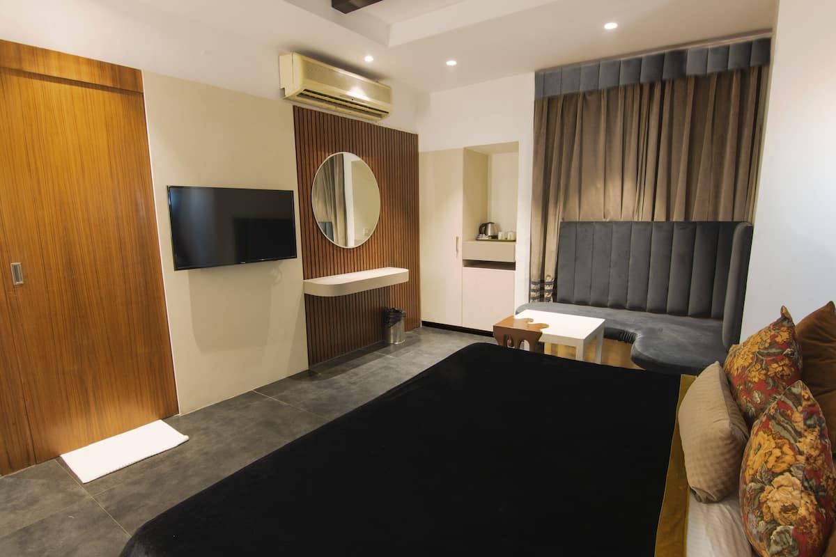 Une chambre d’hôtel moderne dotée d’un grand lit, d’une télévision, d’un petit bureau et d’un coin salon avec un canapé et des rideaux.