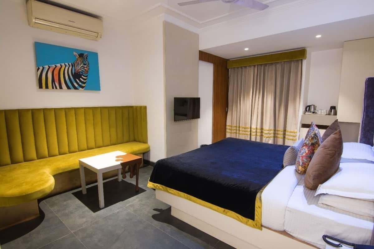Une chambre d’hôtel avec un lit, un canapé, une petite table, une télévision et un tableau représentant une zèbre.