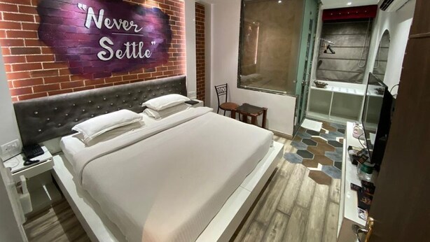 A modern hotel room with a large bed, a vanity with a mirror, a small table, and a shower area. - Hotel Sri Nanak Continental (New Delhi)