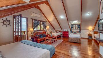 A spacious attic bedroom with a large bed, a wooden desk, and a cozy seating area.