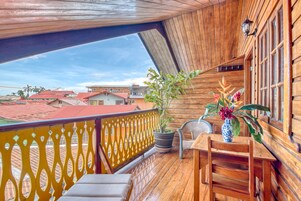 Un balcón de madera con vistas a casas, una planta en maceta y una mesa con sillas.