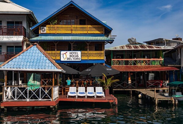 Un hotel con un letrero que dice "Hotel Bocas Del Toro" sobre una estructura flotante, con asientos al aire libre y un área cubierta.