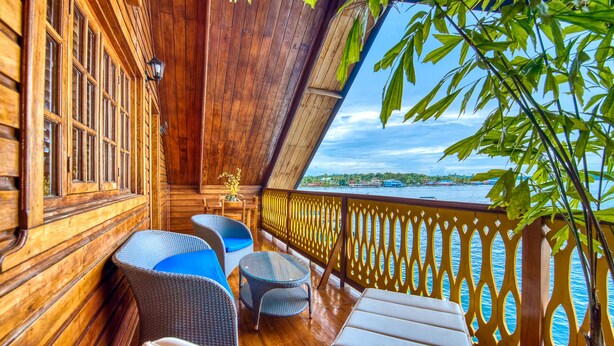 Una terraza de madera con mobiliario de mimbre, vistas al agua y una barandilla decorativa.