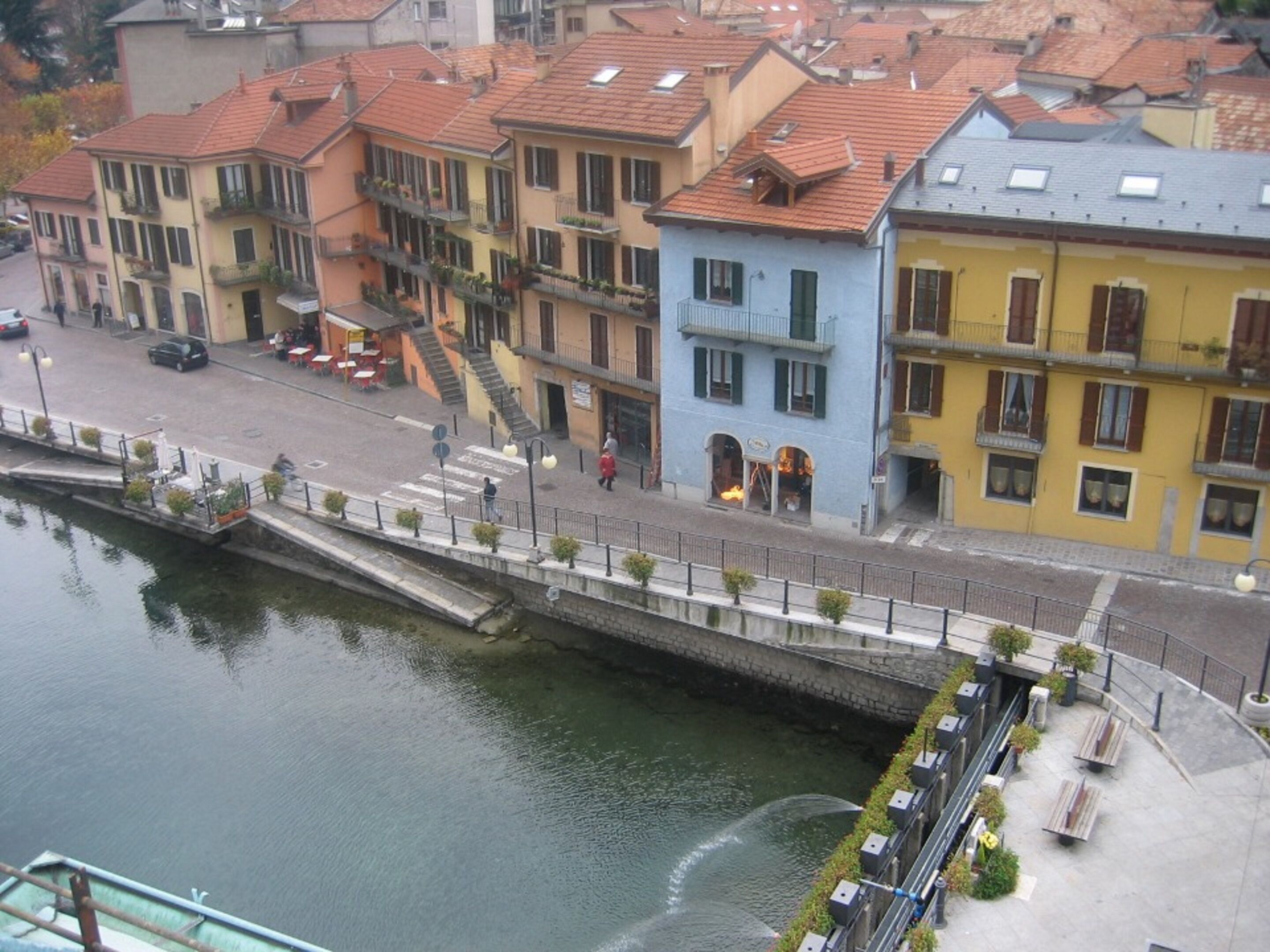 A canal-side building with a staircase leading to a second-floor balcony, a row of benches along the water, and a pedestrian walkway.